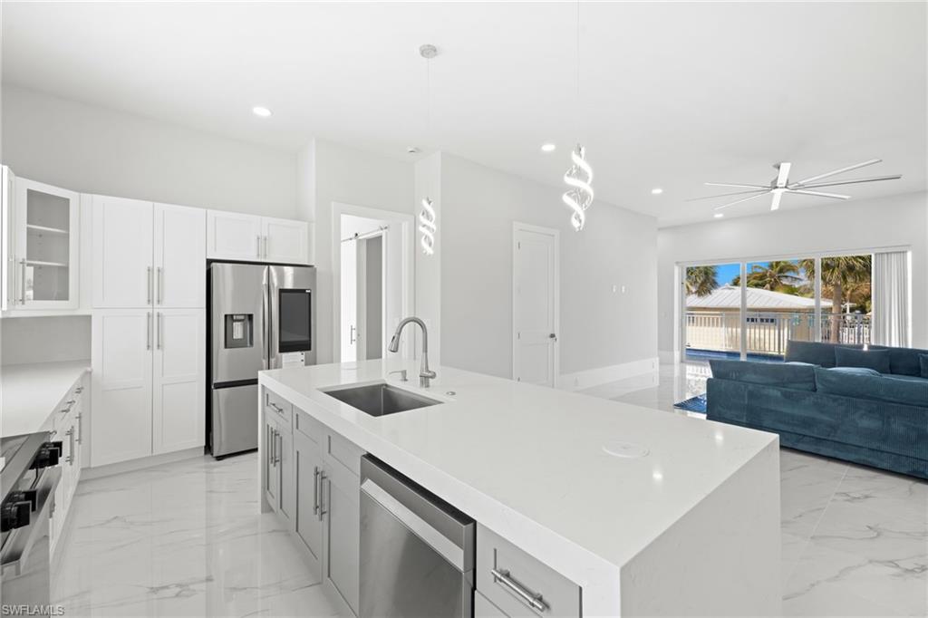 Kitchen with glass fronted cabinets, stainless steel appliances, a kitchen island with sink, and white cabinetry