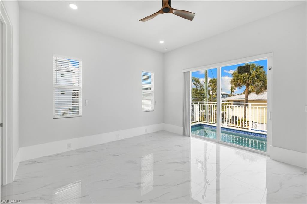 Spare room featuring a ceiling fan, healthy amount of natural light, light marble finish flooring, and recessed lighting