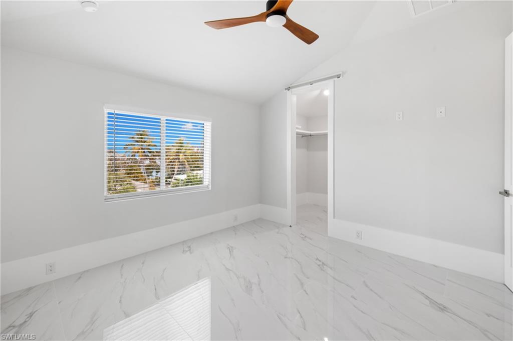 Unfurnished bedroom with a spacious closet, ceiling fan, vaulted ceiling, and light marble finish floors