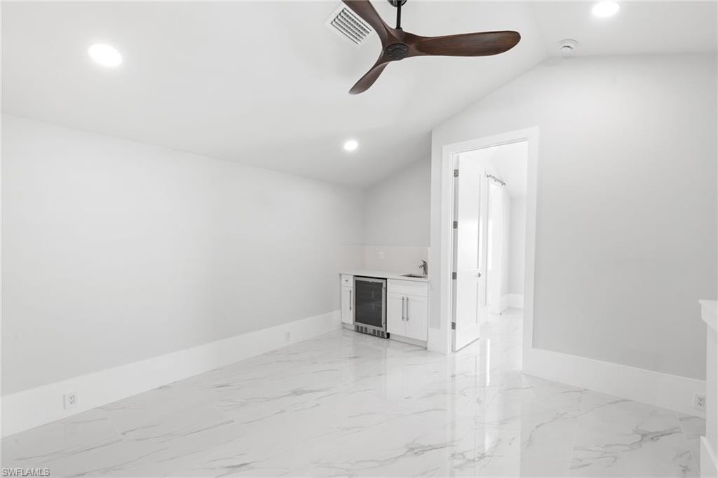 Unfurnished room with beverage cooler, recessed lighting, a ceiling fan, light marble finish flooring, and lofted ceiling