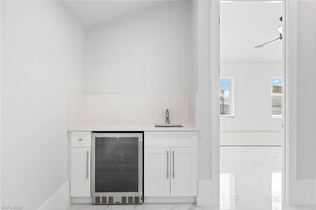 Indoor wet bar with beverage cooler, white cabinetry, light marble finish floors, and light stone counters