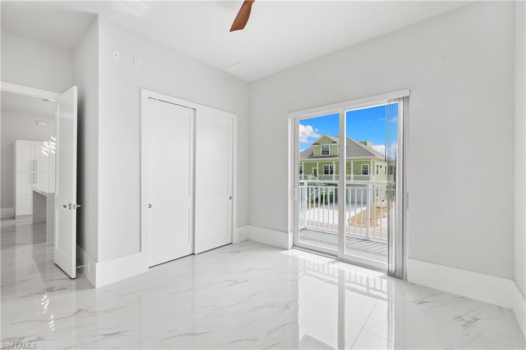 Unfurnished bedroom featuring light marble finish floors, a closet, access to exterior, and a ceiling fan
