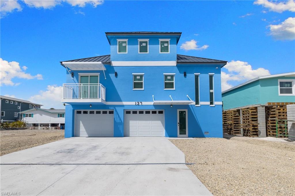 Coastal home with a standing seam roof, a balcony, stucco siding, concrete driveway, and an attached garage