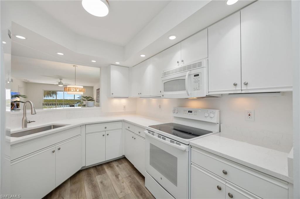 Kitchen featuring white appliances, white cabinets, light wood finished floors, hanging light fixtures, and a ceiling fan