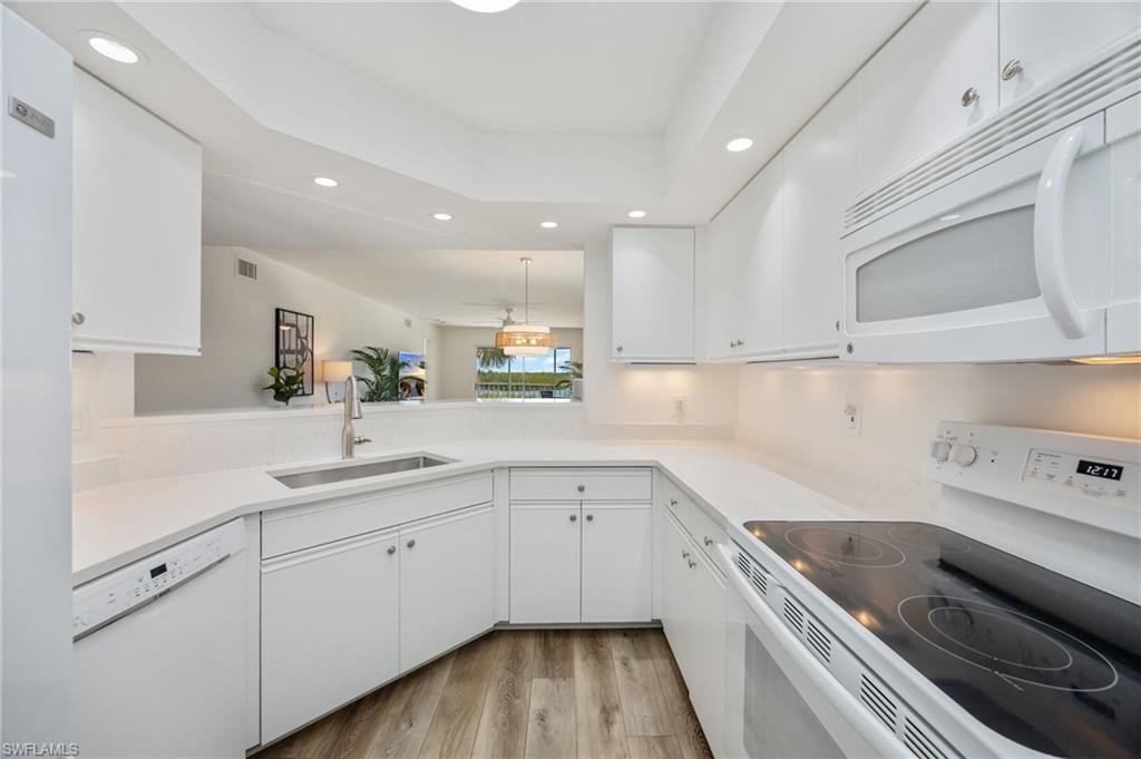 Kitchen with white appliances, recessed lighting, white cabinets, a tray ceiling, and light wood-style floors