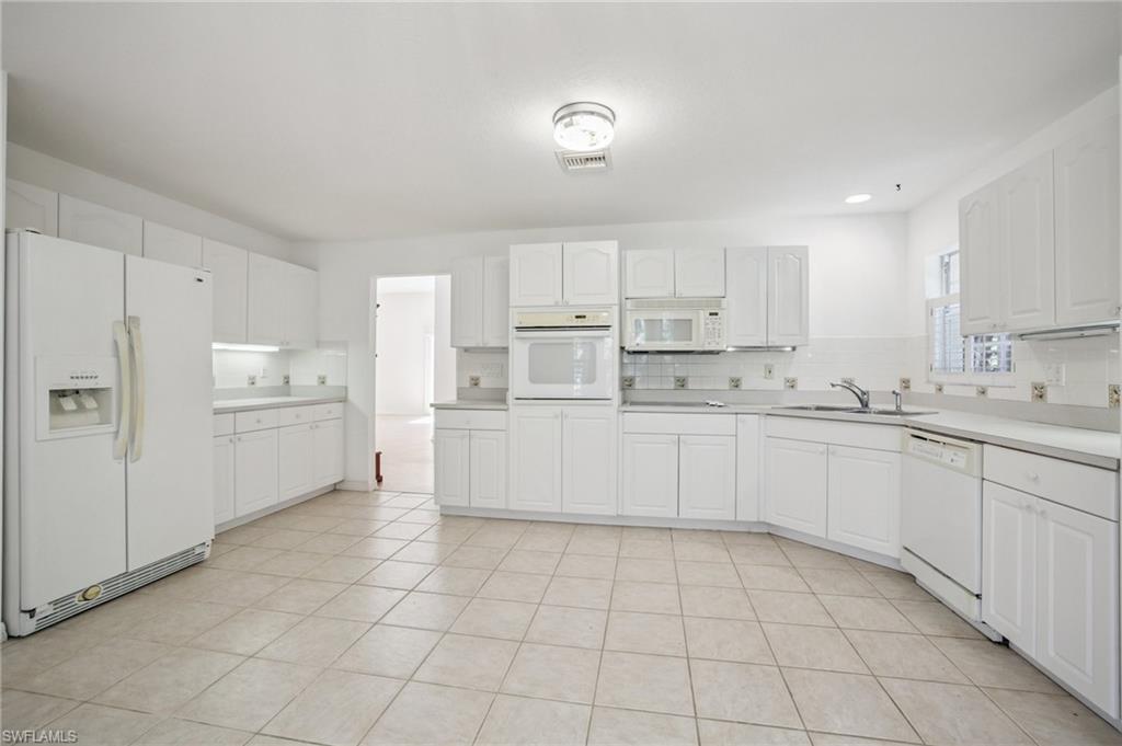 Kitchen with white appliances, backsplash, white cabinets, and light countertops