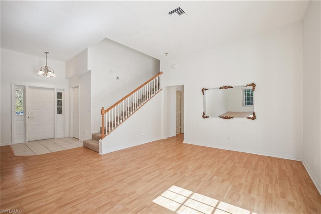 Foyer with light wood laminate flooring, a high ceiling, and hanging lights