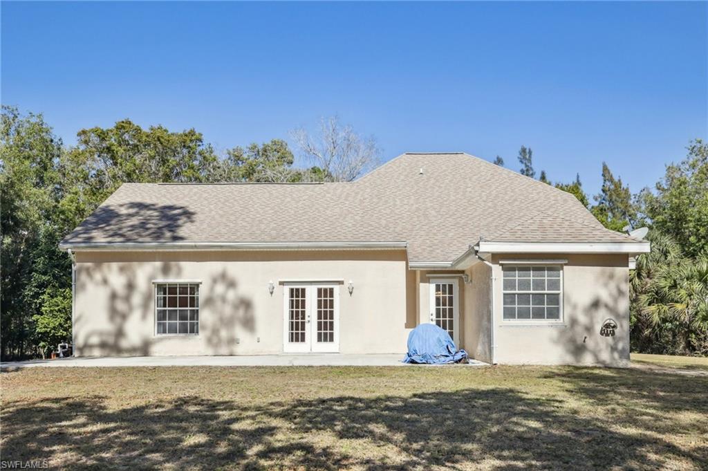 Rear view of property with French doors, stucco siding, a shingled roof, and lawn