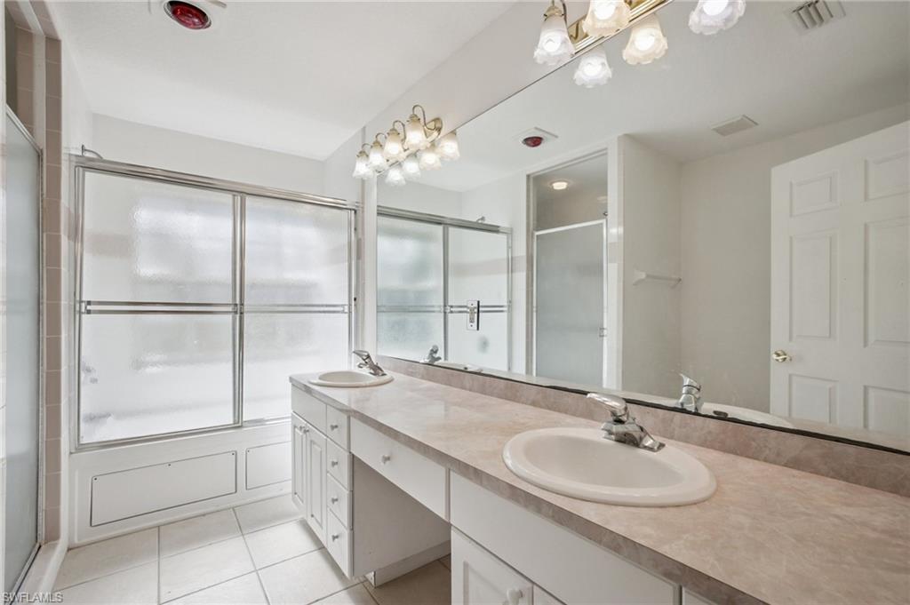 Full bath featuring double vanity, light tile patterned flooring, and an enclosed shower