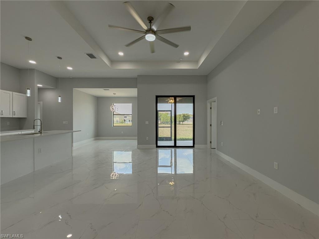 Empty room with a tray ceiling, a ceiling fan, visible vents, marble finish floor, and baseboards