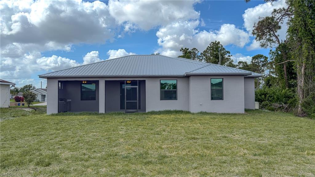 Rear view of house featuring stucco siding, a yard, and metal roof