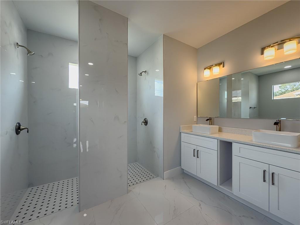 Full bath with a marble finish shower, double vanity, marble finish floor, and a sink