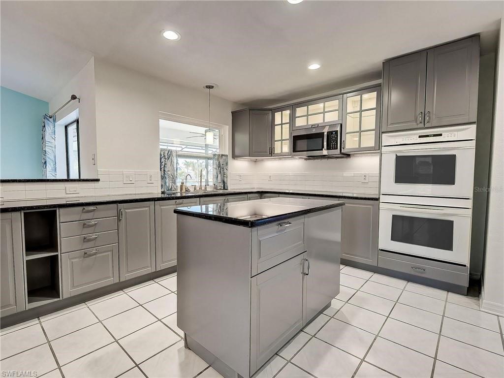 Kitchen with gray cabinets, tasteful backsplash, double oven, a center island, and light tile patterned floors