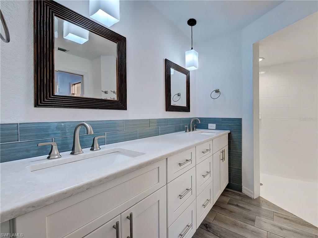 Bathroom with double vanity, dark wood finished floors, a tile shower, and tile walls