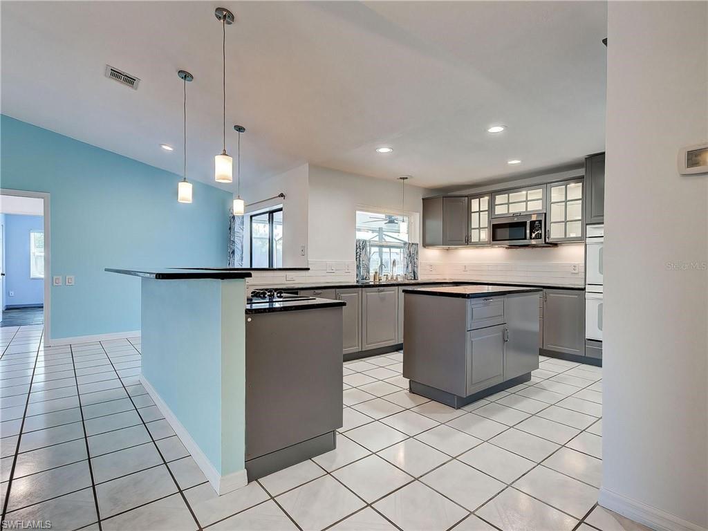 Kitchen featuring gray cabinetry, dark countertops, a center island, decorative light fixtures, and a peninsula