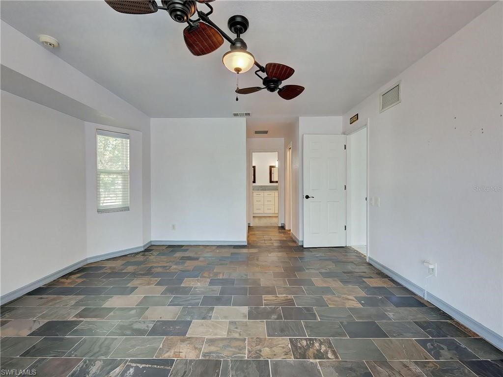 Unfurnished bedroom with ceiling fan, ensuite bath, and dark stone finish flooring
