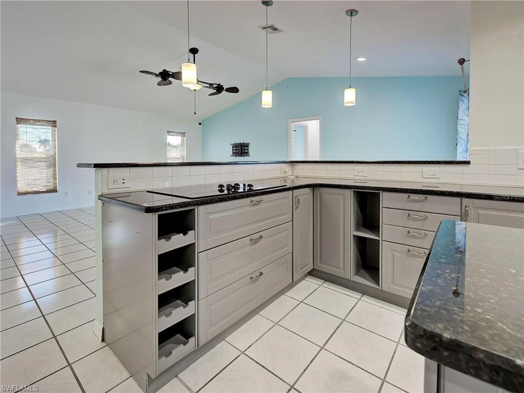 Kitchen with open shelves, dark stone counters, light tile patterned floors, a ceiling fan, and decorative light fixtures