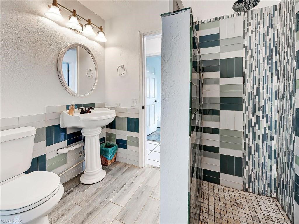 Full bathroom featuring tile walls, a tile shower, wainscoting, and wood tiled floors
