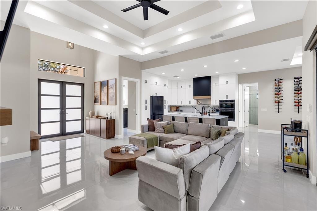 Living area with a tray ceiling, a ceiling fan, french doors, and recessed lighting