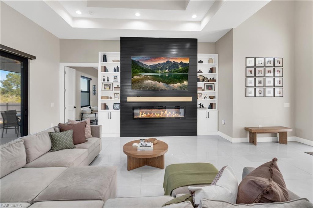 Living area with tile patterned floors, a large fireplace, recessed lighting, built in shelves, and a raised ceiling