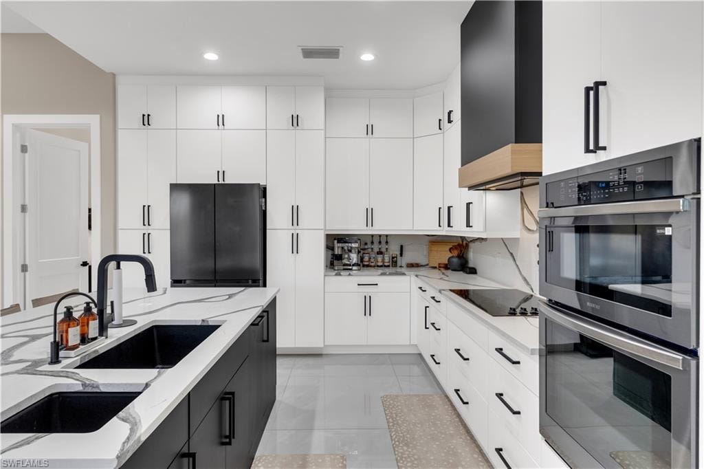 Dual tone kitchen with black appliances, dual tone cabinetry, light stone countertops, modern cabinets, and recessed lighting