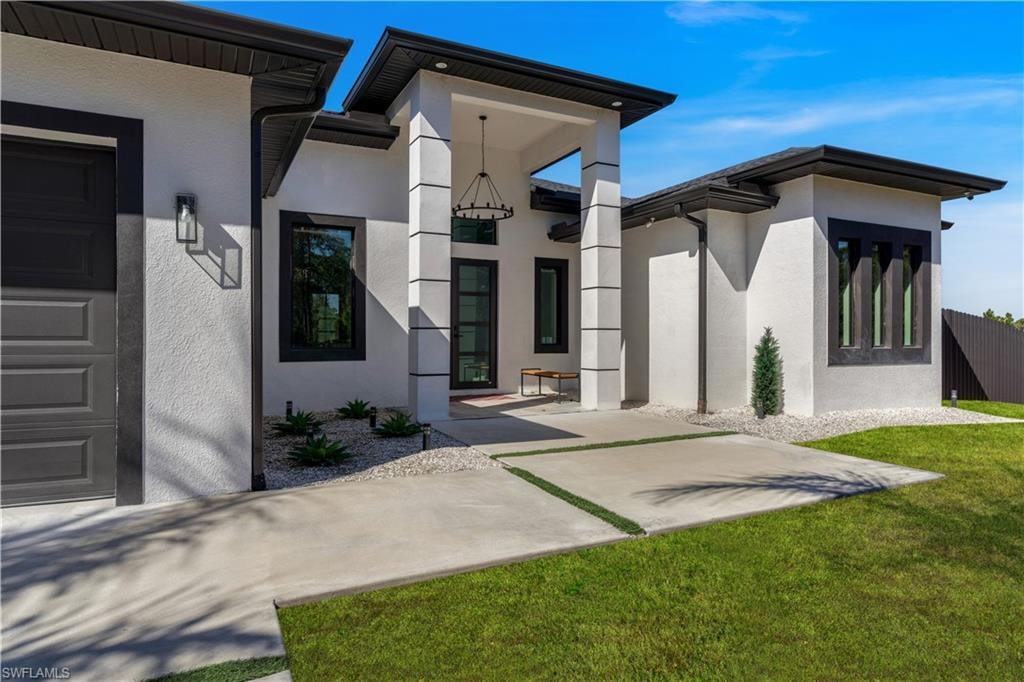Entrance to property featuring stucco siding, a lawn, and a garage