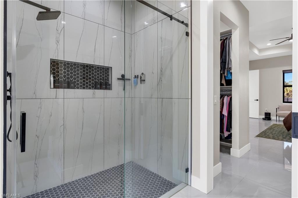 Full bathroom with a marble finish shower, a walk in closet, ceiling fan, tile patterned flooring, and a raised ceiling
