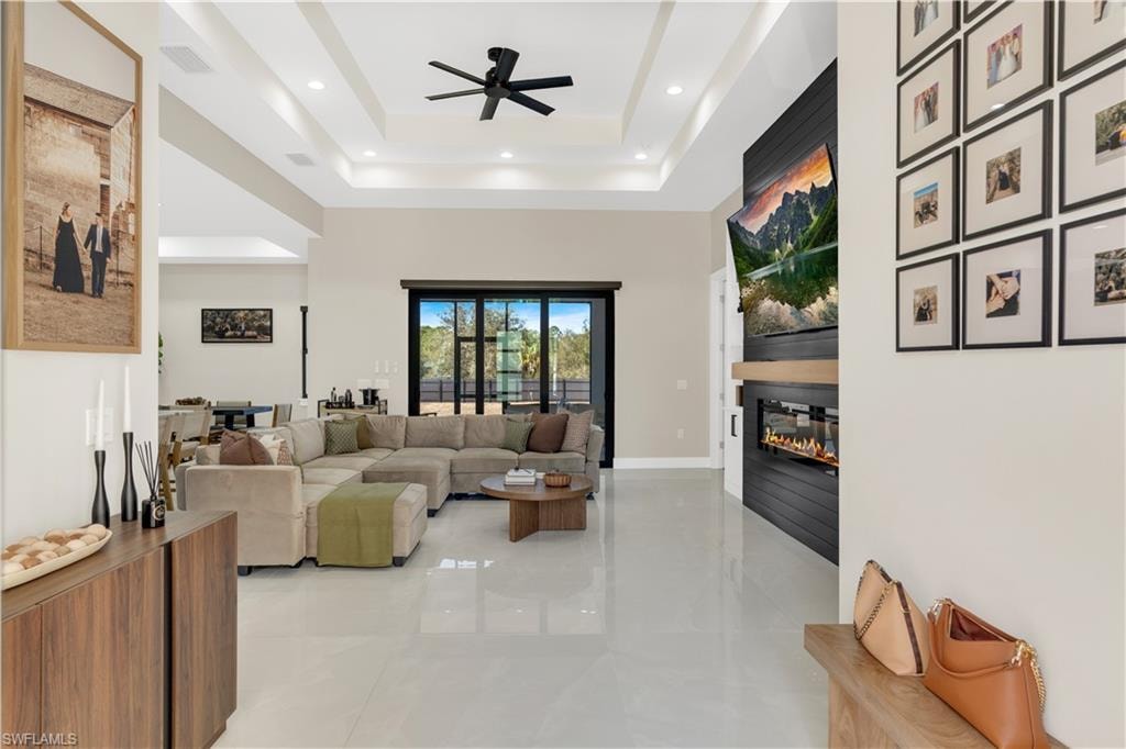 Living room with a fireplace, ceiling fan, a high tray ceiling, and recessed lighting