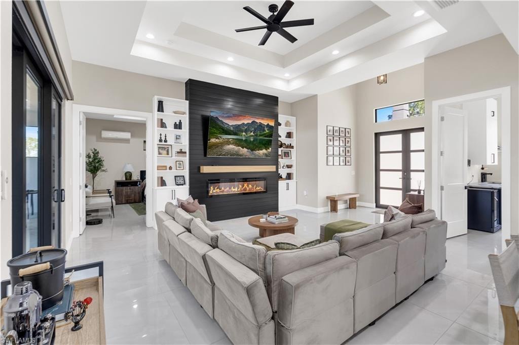 Living room with a ceiling fan, plenty of natural light, a large fireplace, a high ceiling, and built in shelves