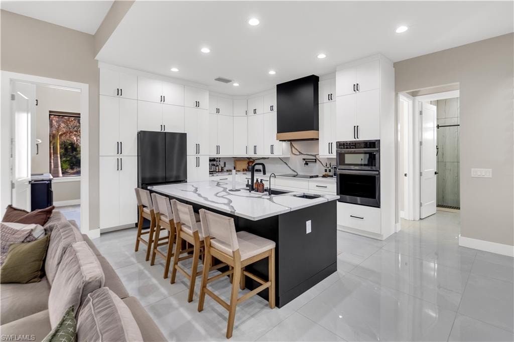 Dual tone kitchen with a center island with sink, a breakfast bar area, double oven, light stone countertops, and two tone cabinetry