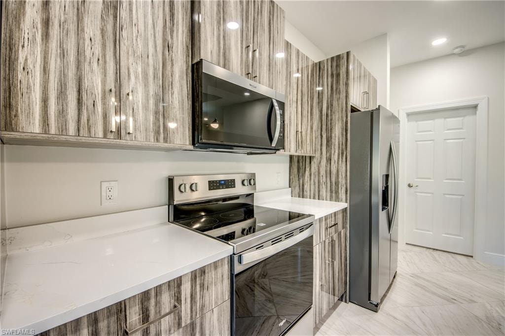 Kitchen with modern cabinets, stainless steel appliances, light stone counters, and recessed lighting