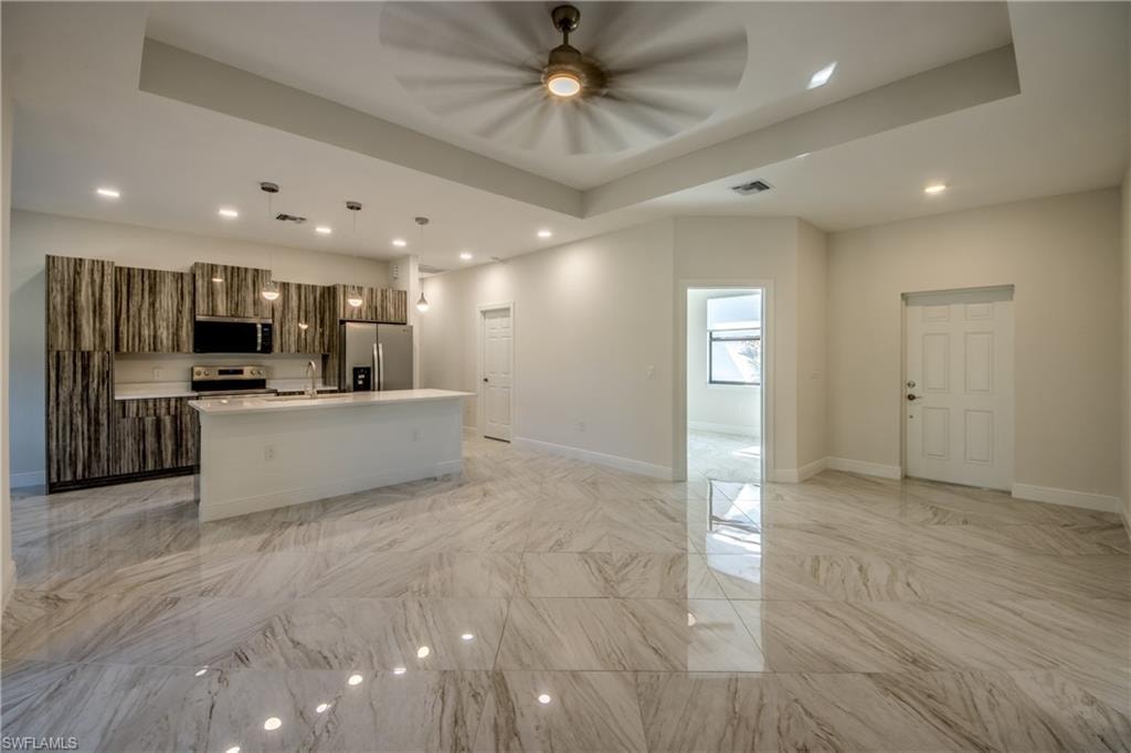Kitchen with a center island with sink, a tray ceiling, open floor plan, pendant lighting, and modern cabinets