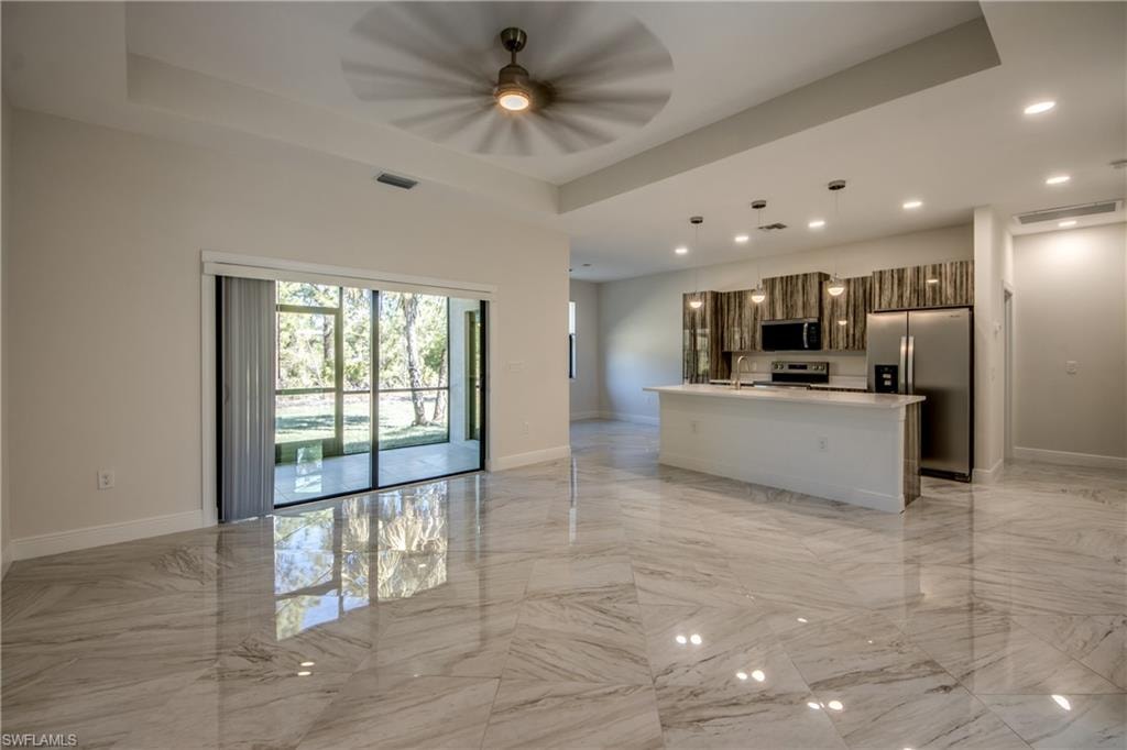 Kitchen featuring open floor plan, a raised ceiling, a kitchen island with sink, stainless steel appliances, and decorative light fixtures