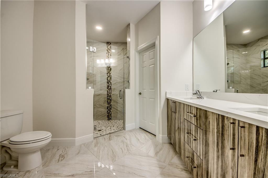 Bathroom featuring double vanity, a marble finish shower, light marble finish flooring, and recessed lighting