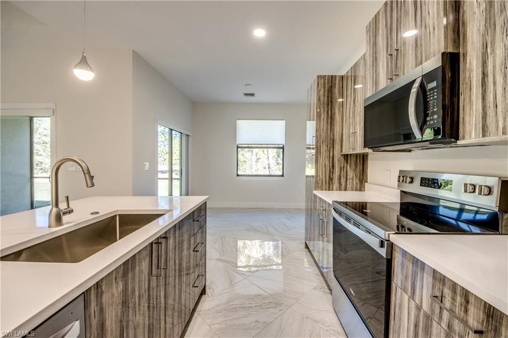 Kitchen featuring stainless steel appliances, modern cabinets, pendant lighting, light stone counters, and light marble finish flooring