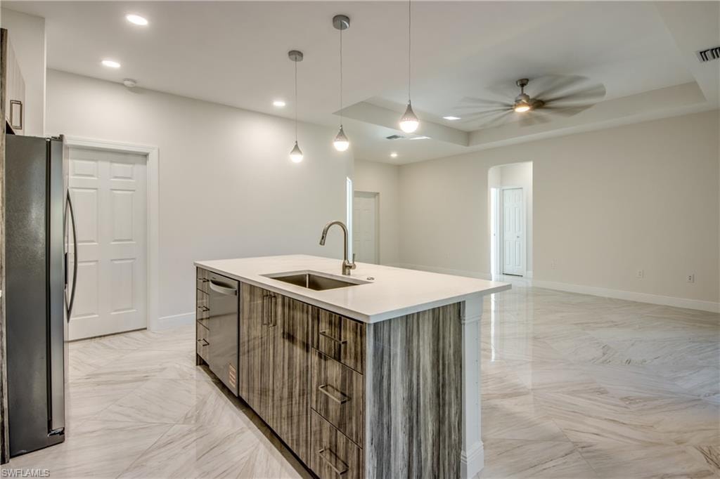 Kitchen featuring stainless steel appliances, hanging light fixtures, open floor plan, an island with sink, and a ceiling fan