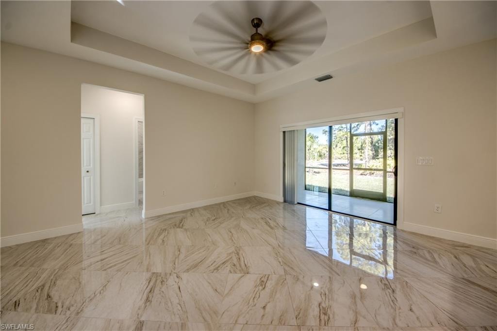 Empty room with a tray ceiling, light marble finish floors, and a ceiling fan