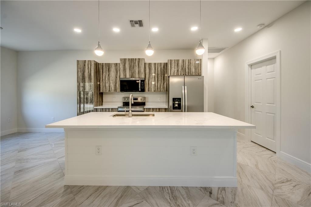 Kitchen with stainless steel appliances, light stone countertops, a center island with sink, pendant lighting, and modern cabinets