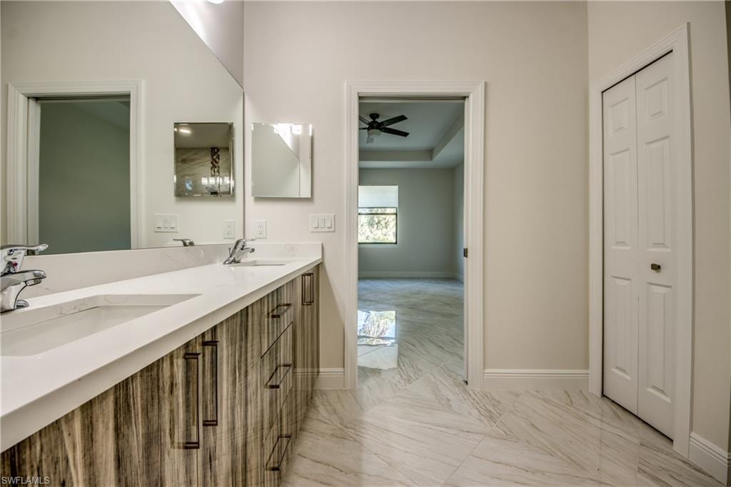 Bathroom with double vanity, light marble finish floors, and a ceiling fan