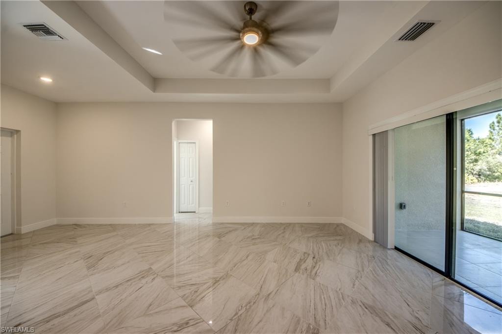 Empty room with ceiling fan, a tray ceiling, and recessed lighting