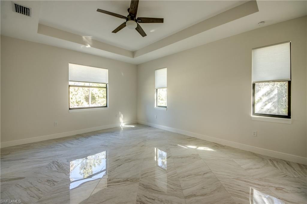 Empty room with a tray ceiling, ceiling fan, and light marble finish flooring