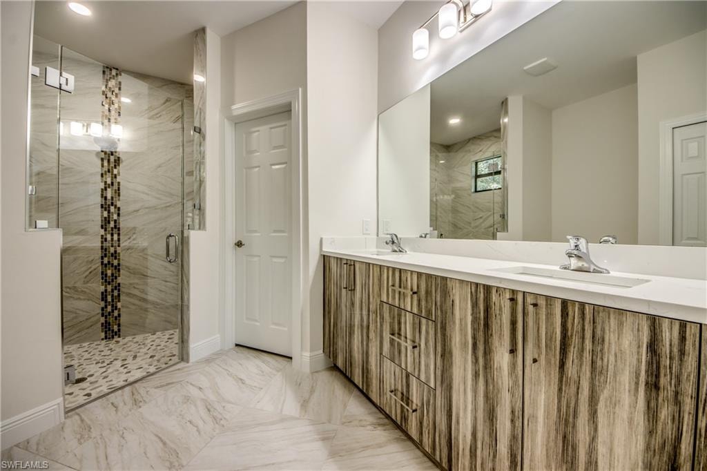 Bathroom featuring a marble finish shower, double vanity, and light marble finish floors