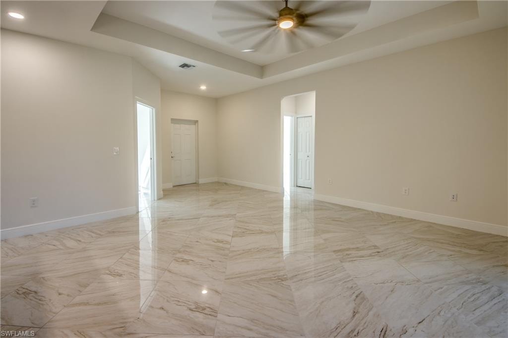 Spare room featuring a raised ceiling, recessed lighting, arched walkways, a ceiling fan, and light marble finish floors
