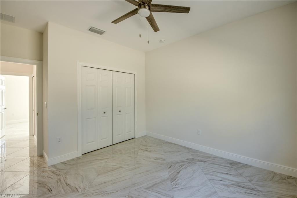 Unfurnished bedroom with a ceiling fan, light marble finish flooring, and a closet