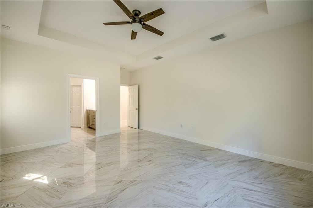 Spare room with a tray ceiling, light marble finish flooring, and a ceiling fan