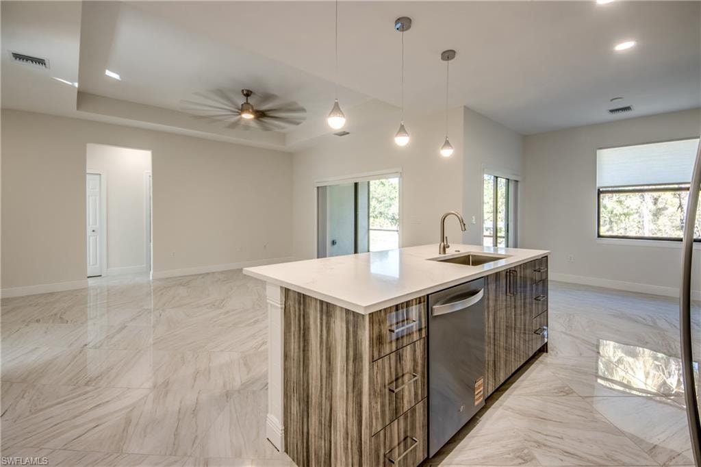 Kitchen with open floor plan, hanging light fixtures, dishwasher, wood finish cabinets, and a raised ceiling