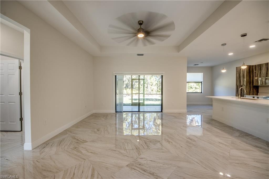 Unfurnished living room with light marble finish floors, a ceiling fan, and a raised ceiling