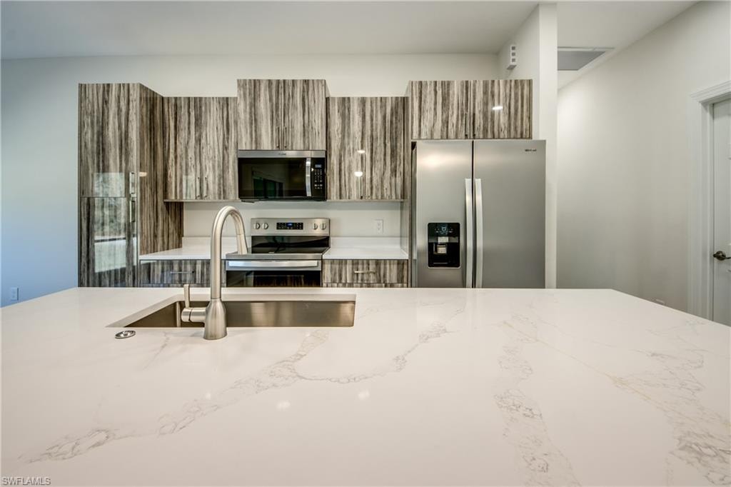 Kitchen with wood finish cabinetry, stainless steel appliances, light stone counters, and modern cabinets