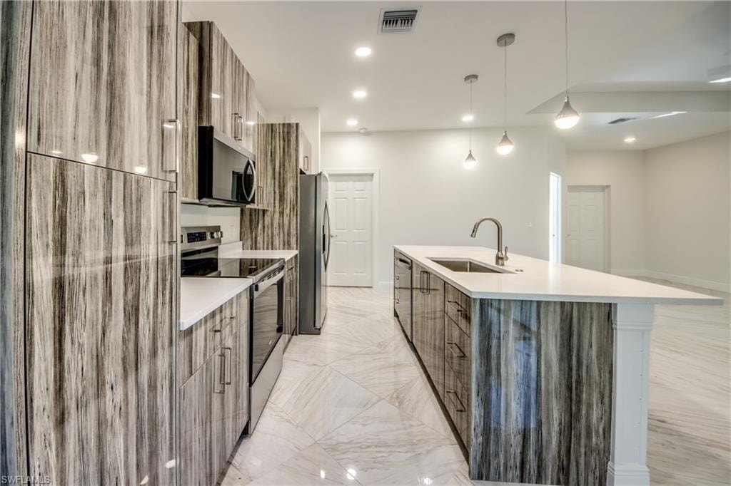 Kitchen featuring modern cabinets, stainless steel appliances, a center island with sink, pendant lighting, and light stone countertops