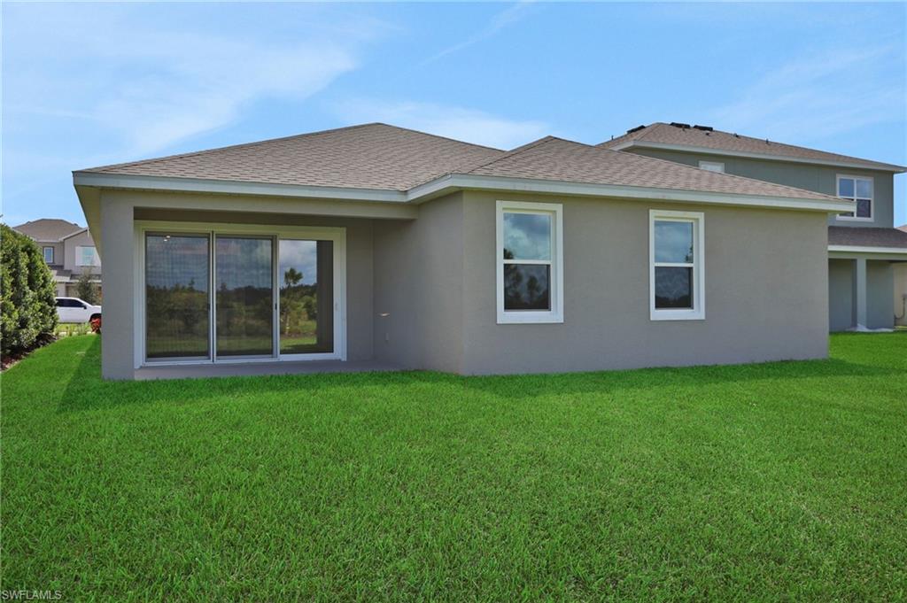 Rear view of house featuring roof with shingles, stucco siding, and a yard
